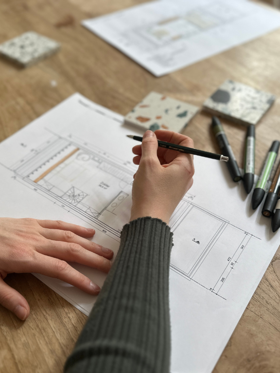 mains de femme dessinant un plan d'architecture sur une table en bois