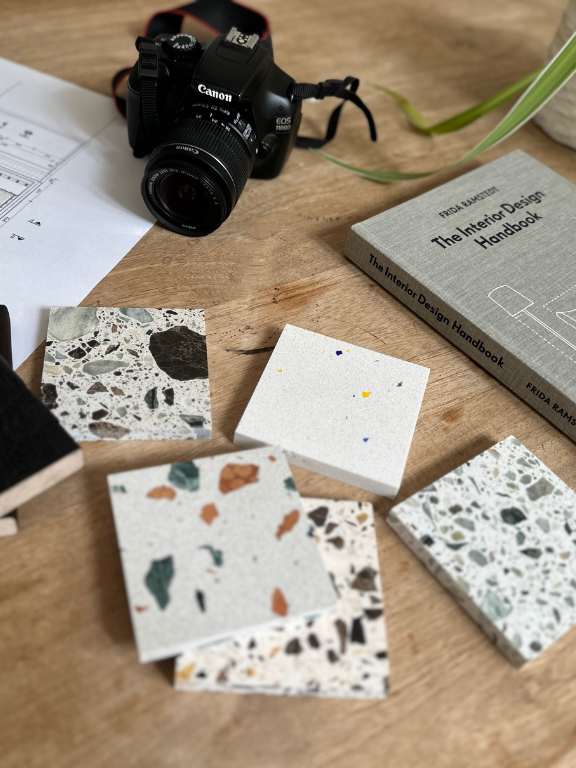 échantillons de carrelages de décoration, livre d'architecture et appareil photo sur une table en bois